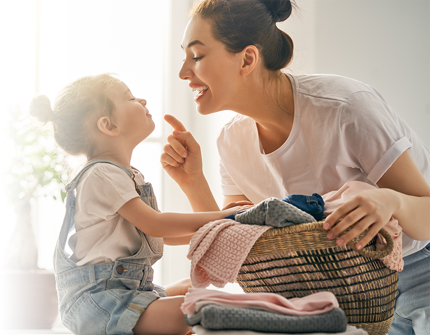Mother and daughter putting laundry in the basket together.